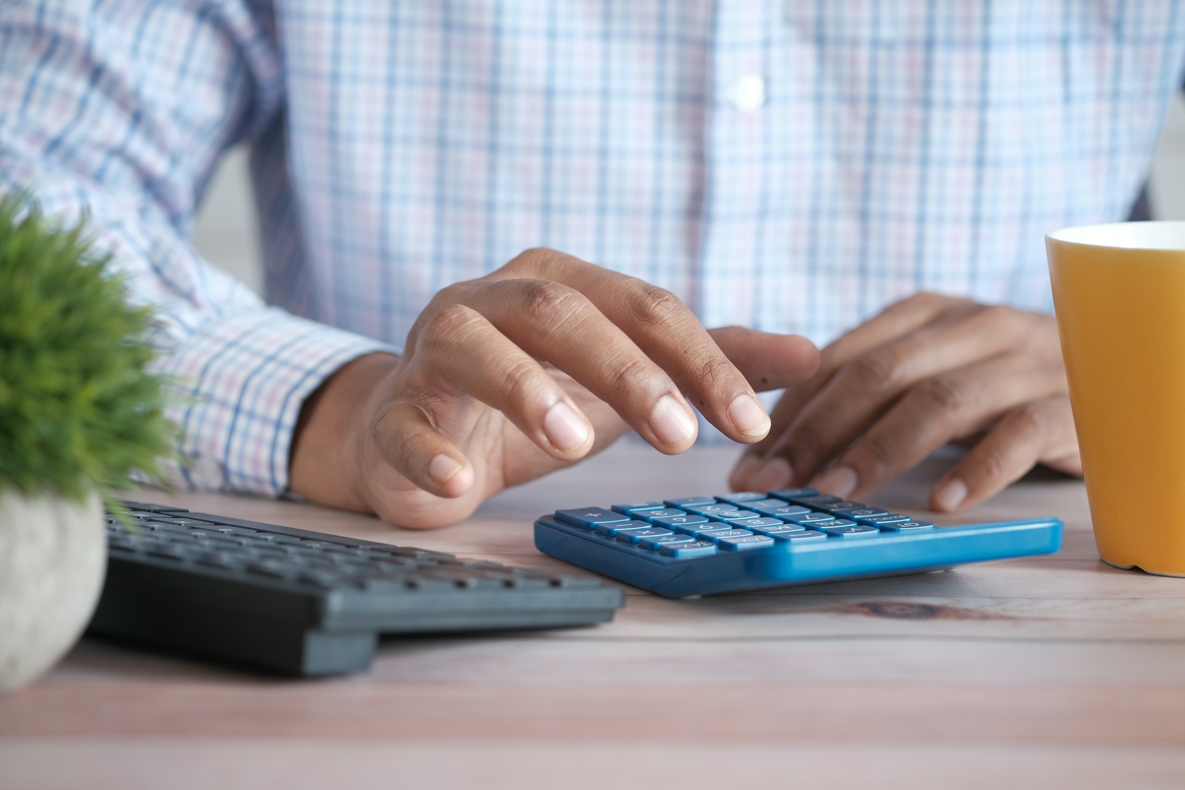 Mão usando calculadora azul sobre a mesa ao refazer a conta da precificação de agência