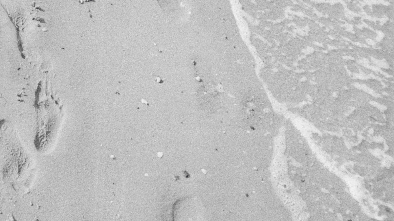 Pegadas na areia sumindo na onda, metáfora do rastro que a atribuição de marketing perde quando a jornada passa pela IA