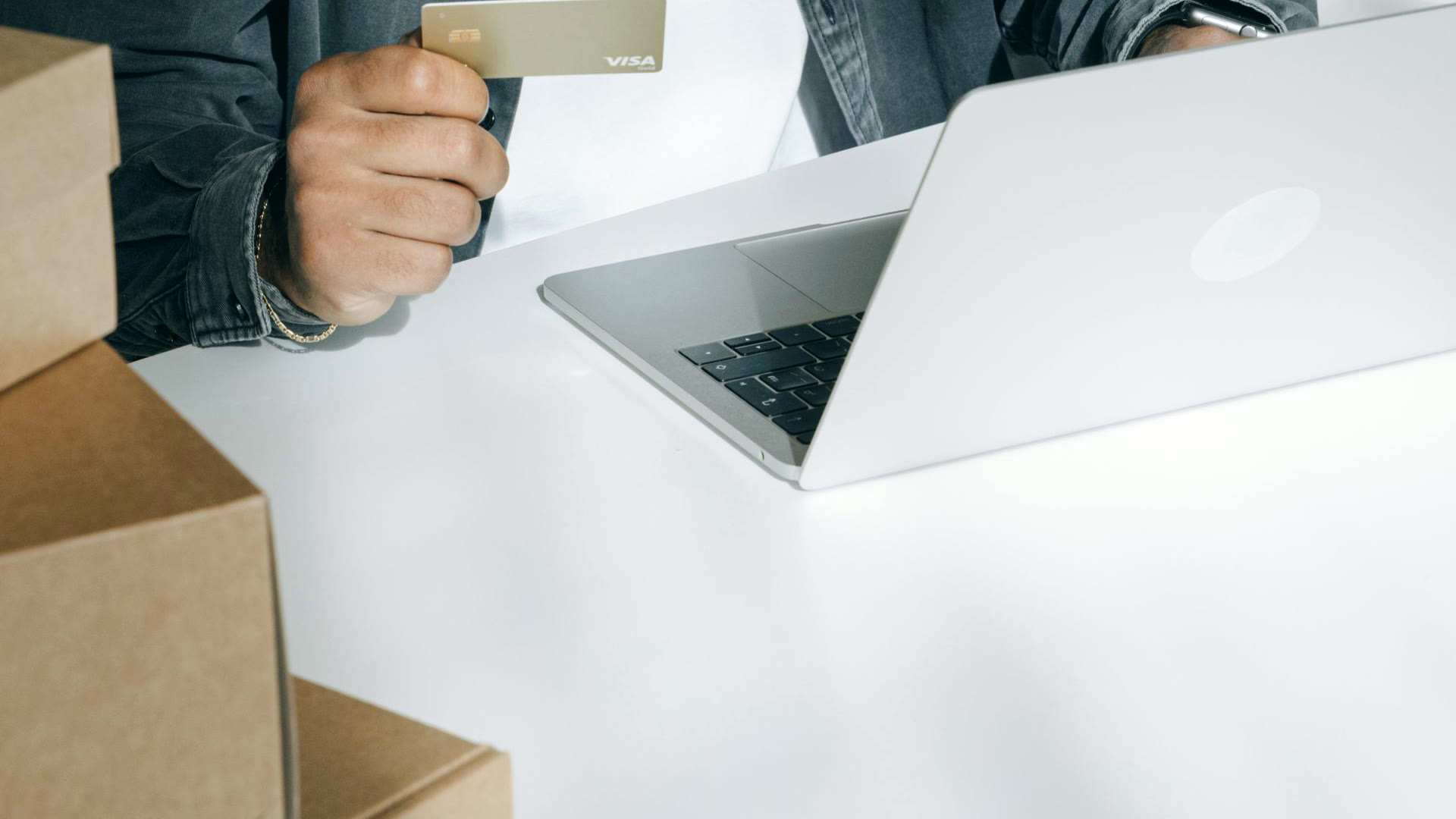 Pessoa com cartão de crédito na mão diante do notebook, cercada de caixas de envio, a compra online que a campanha de Black Friday precisa converter