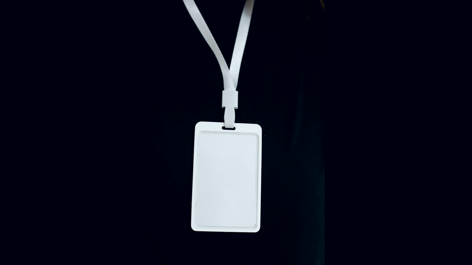 Crachá em branco pendurado num cordão sobre fundo preto, imagem do onboarding de agentes de IA que ganham identidade própria na empresa