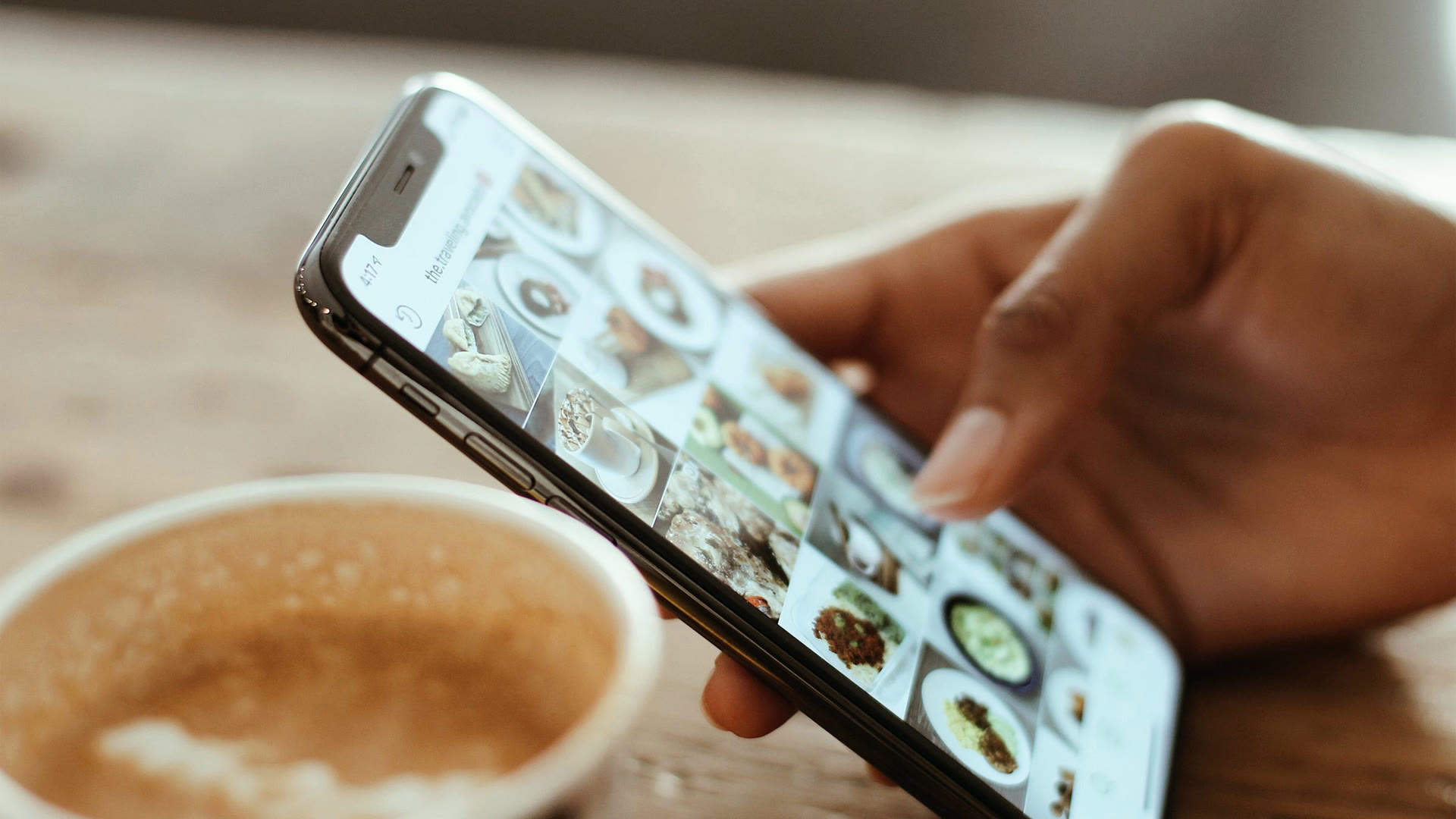 Mão rolando o feed do Instagram no celular ao lado de um café, o público que decide em segundos se o post de social media com IA parece genérico