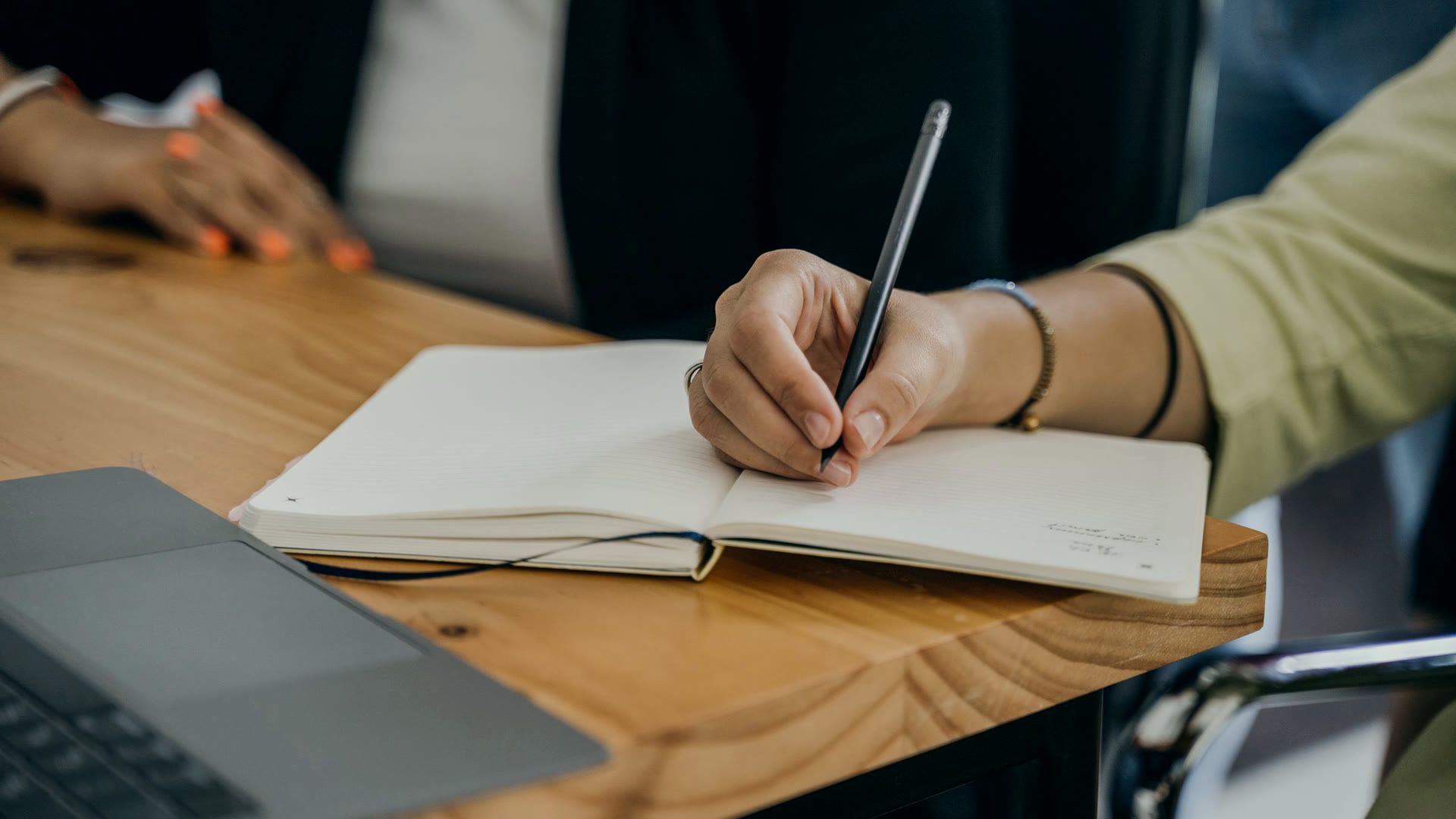 Mão escrevendo anotações num caderno ao lado do notebook, a revisão humana que o Google pede no SEO com IA