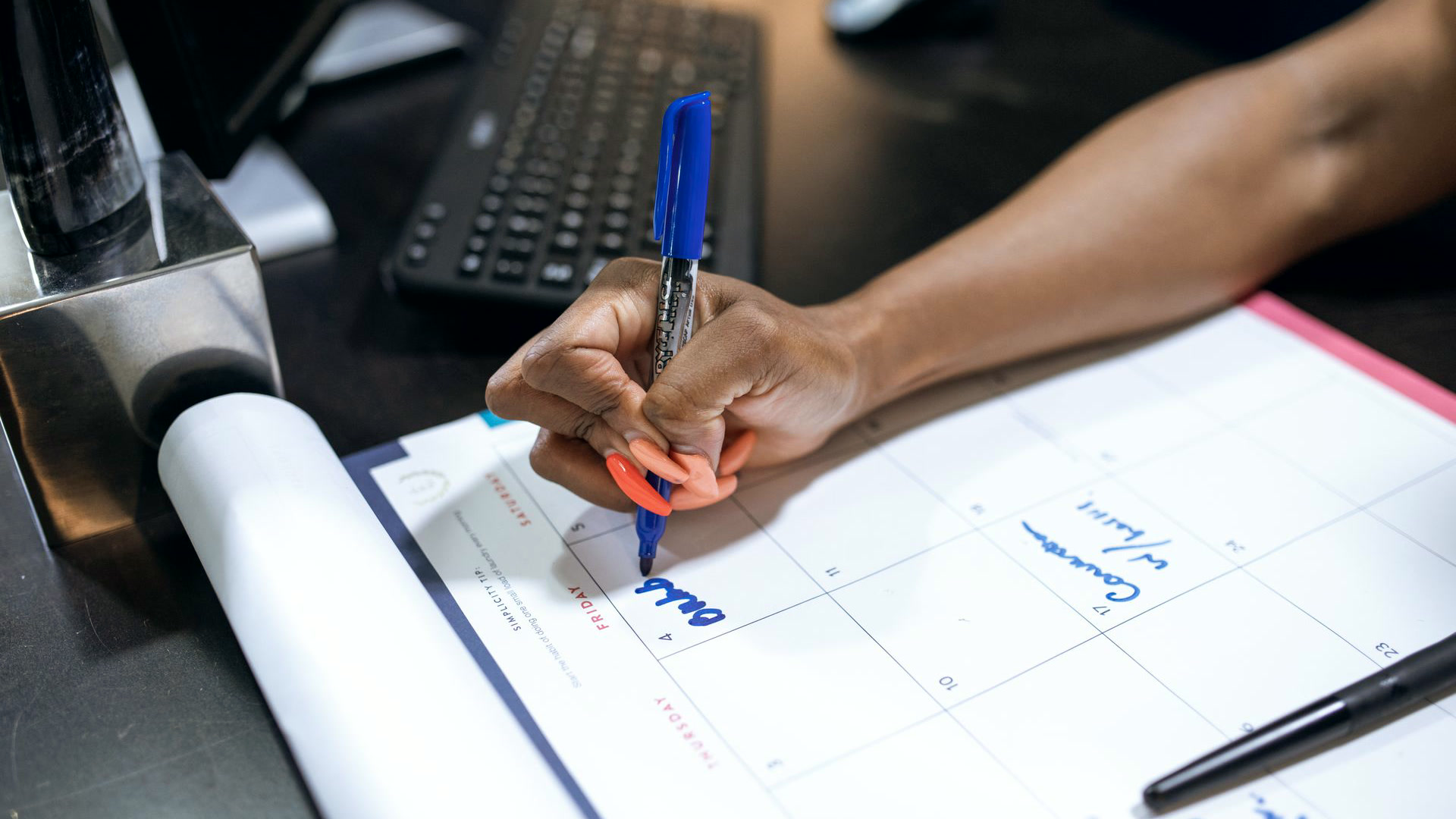 Mão anotando compromissos com caneta azul num calendário de mesa, o ponto de partida do planejamento de marketing para 2027