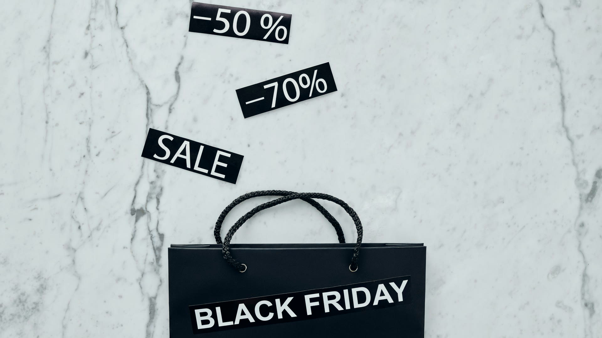Sacola preta escrita Black Friday e etiquetas de 50% e 70% de desconto sobre mármore, a oferta que a campanha de Black Friday precisa sustentar