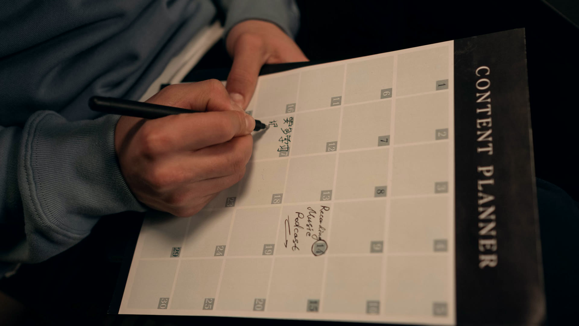 Mão escrevendo num planner de conteúdo mensal, a rotina de social media com IA que começa pelo calendário editorial